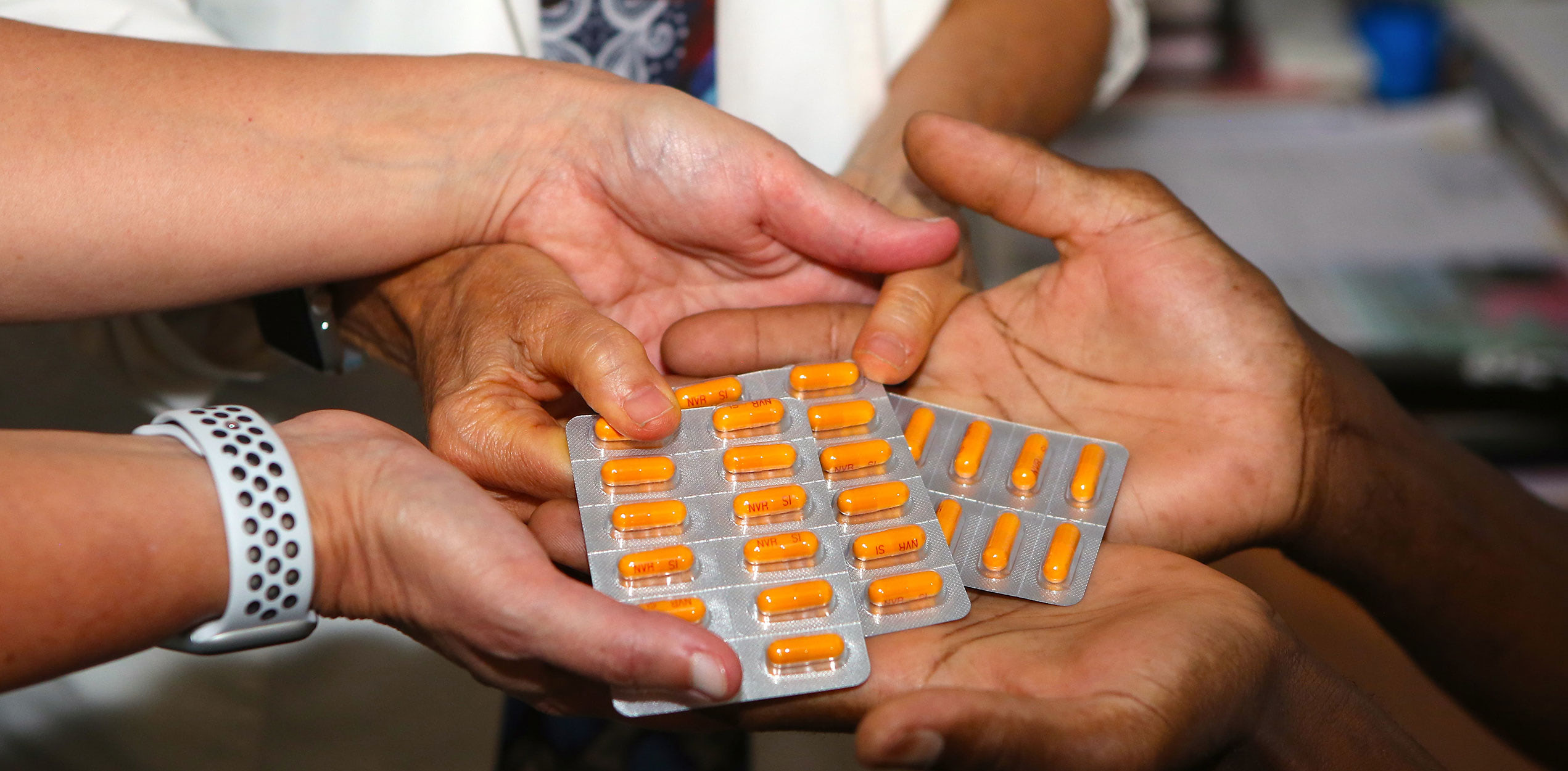 Close-up of one person handing packs of orange medication capsules into another person’s open hands. Access to life-saving treatment and patient support through The Max Foundation.