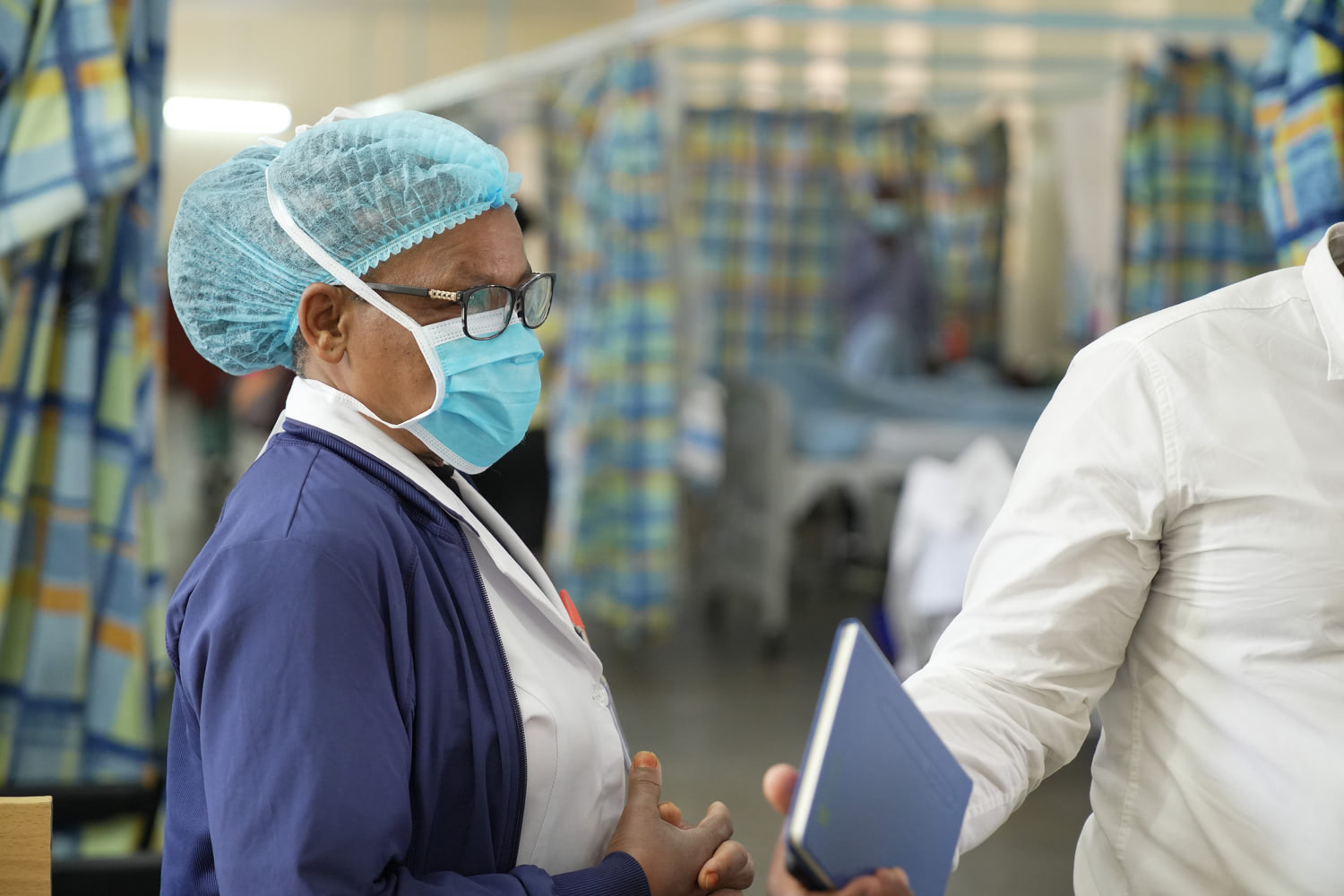 Healthcare working with a mask and medical clothing stands in a hospital speaking with a health partner.